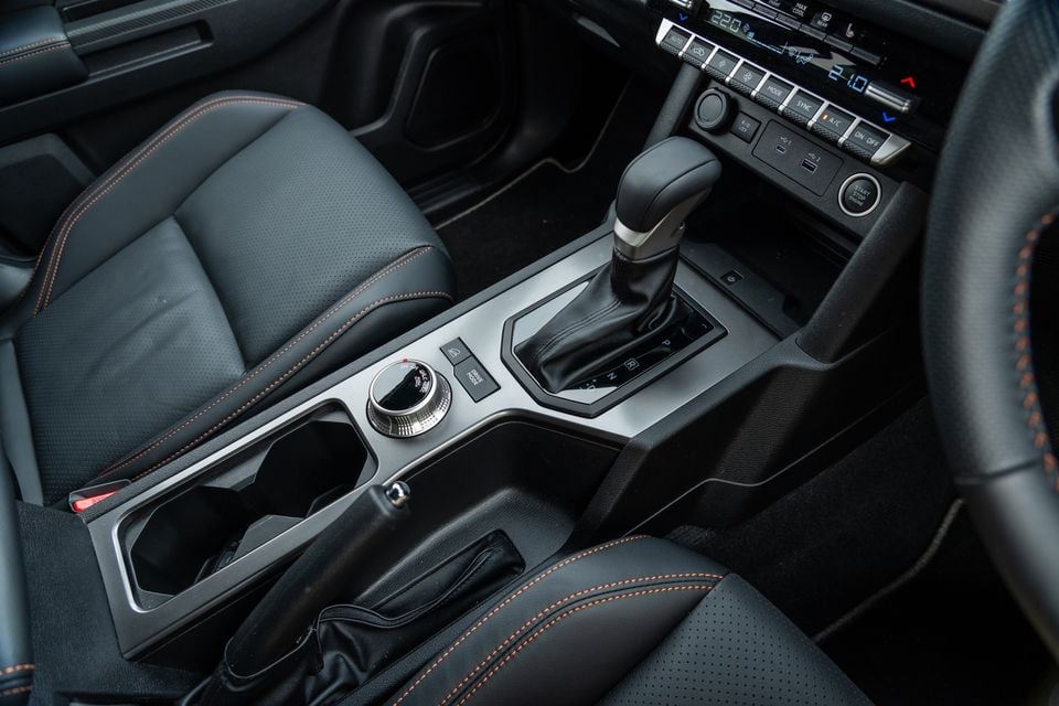Centre console of the 2026 Mitsubishi Triton GSR with gear selector, drive mode dial, handbrake, cupholders and black leather seats with orange stitching