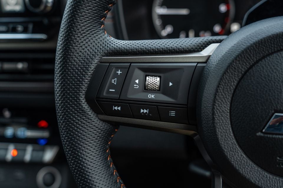 Steering wheel controls in the 2026 Mitsubishi Triton GSR, with volume, media and menu buttons on a leather wheel with orange stitching