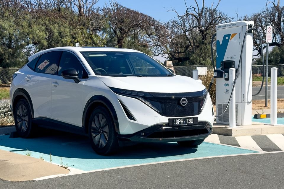 A white Nissan Ariya electric SUV parked at a public fast-charging station in Australia, seen from the front-side