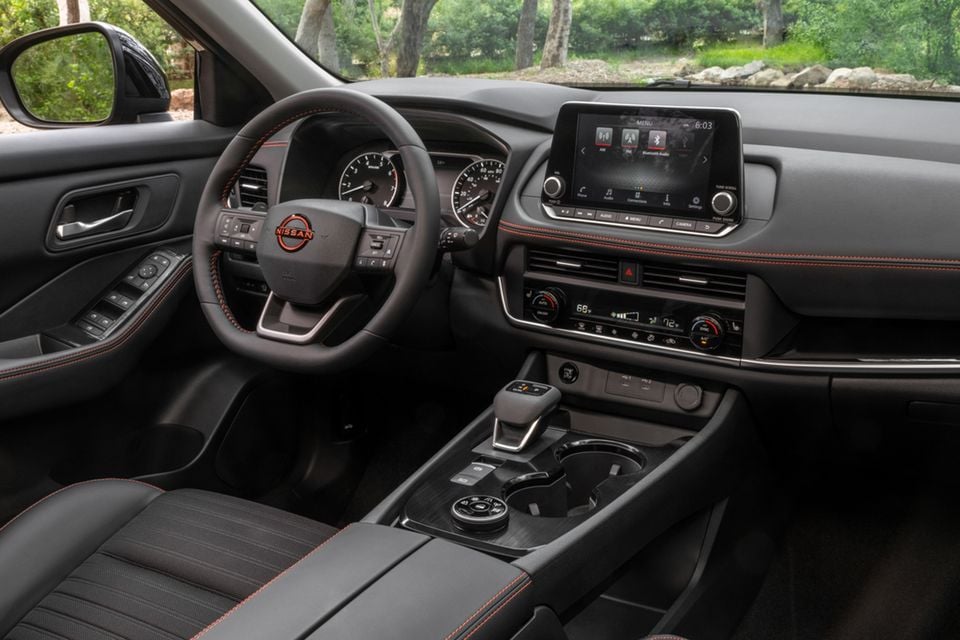 Interior of a 2026 Nissan Rogue Rock Creek Edition showing the dashboard, steering wheel, infotainment screen, centre console and black seats with orange stitching accents