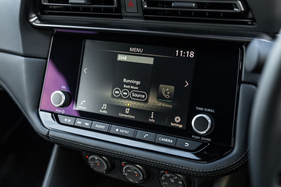 The infotainment touchscreen of a Nissan Z showing the DAB radio menu tuned to Bunnings Rock Music, with physical controls and a tune-scroll dial visible below.