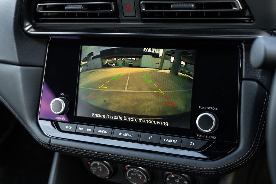 The infotainment screen of a Nissan Z displaying the reversing camera view with coloured guide lines and the message 'Ensure it is safe before manoeuvring'