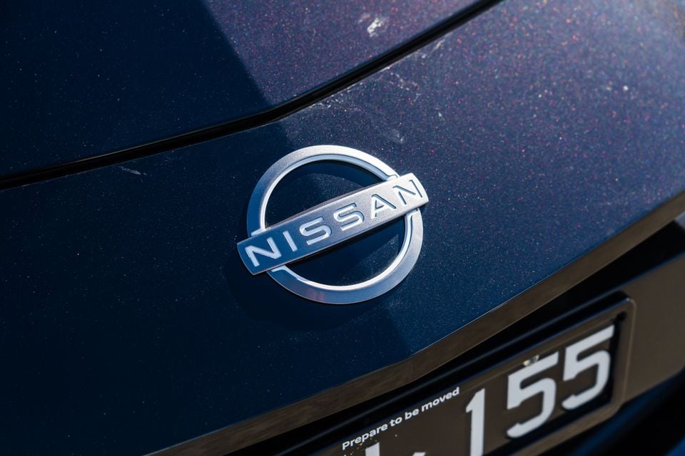 Close-up of the Nissan badge on the rear of a dark blue Nissan Z, with a number plate partially visible below.