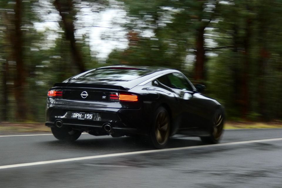 A black Nissan Z coupe seen from the rear, driving on a wet road through a forested area