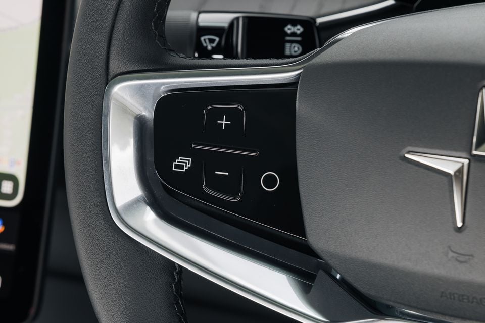 Close-up of the left steering wheel controls on a Polestar 3, showing volume and media buttons with the Polestar logo on the wheel hub