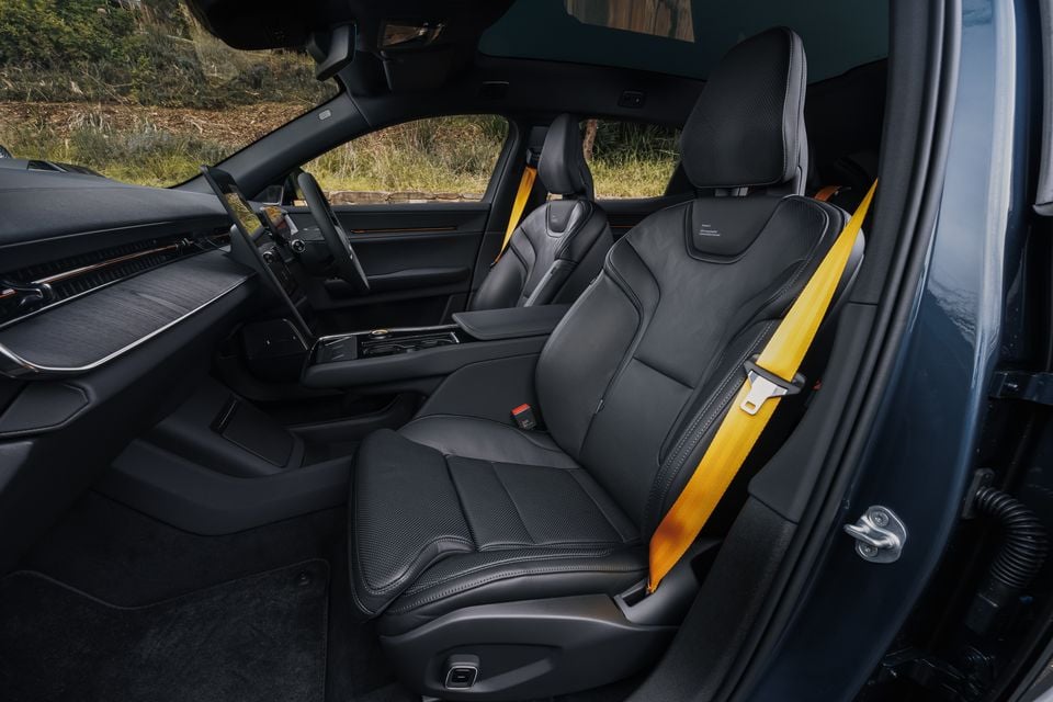 Interior of a 2026 Polestar 3 Performance showing black front seats with yellow seatbelts and orange accents, centre console, and large touchscreen dashboard