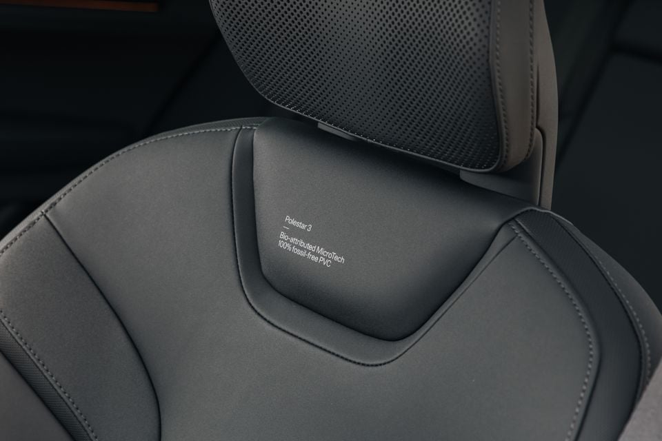 Close-up of a Polestar 3 seat back showing the Bio-attributed MicroTech 100% fossil-free PVC upholstery label embossed on the dark grey material