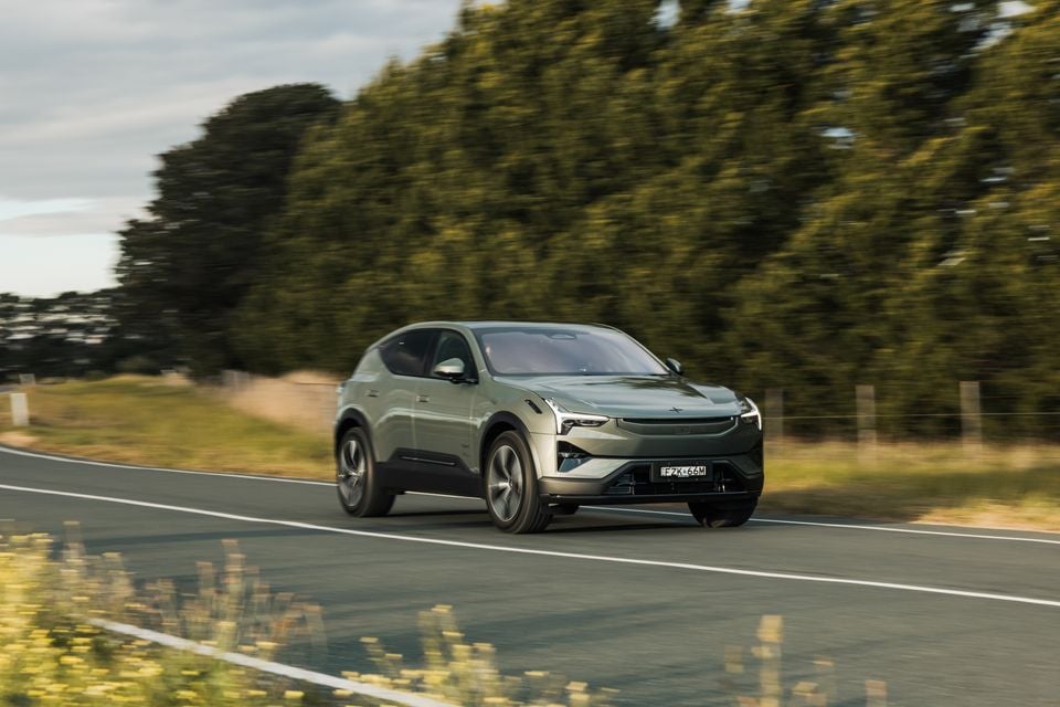 A green Polestar 3 SUV driving on a rural road, seen from the front three-quarter angle