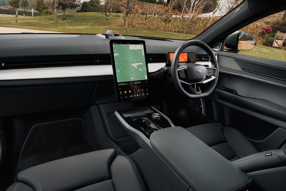 Polestar 3 interior showing the large portrait touchscreen infotainment display, flat-bottom steering wheel, and dark upholstery, viewed from the passenger side