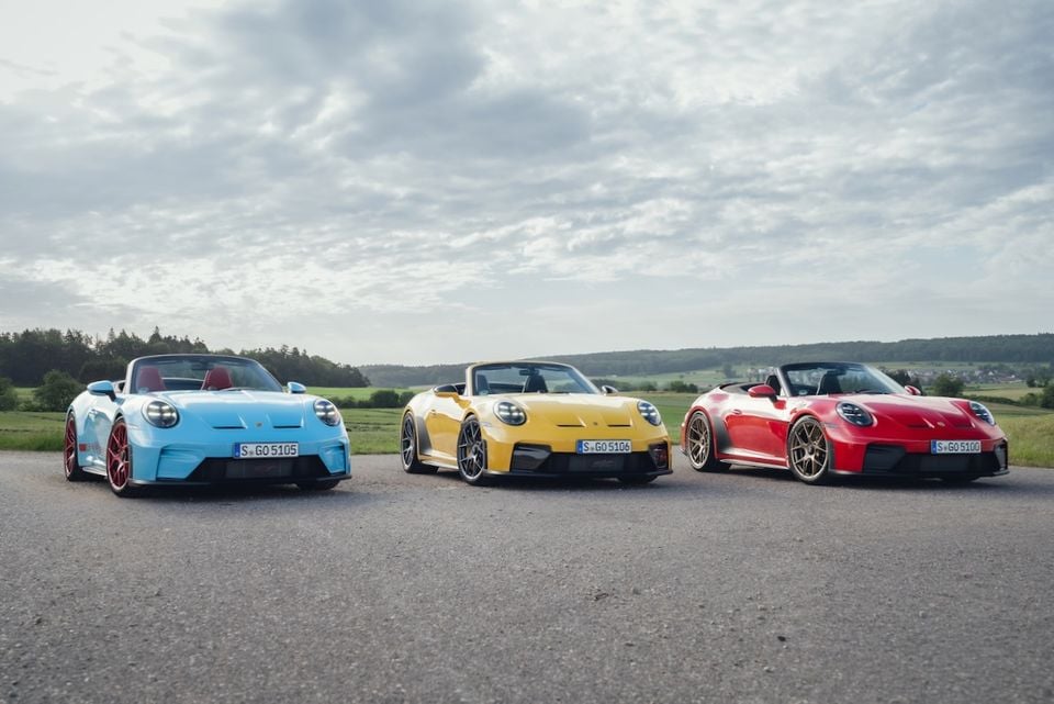 Three Porsche 911 GT3 convertibles parked side by side in blue, yellow, and red, seen from the front on a rural road