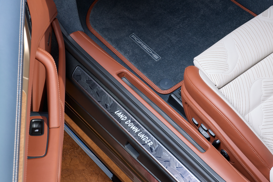 Door sill of a Porsche 911 Turbo S 'Land Down Under' special edition, showing the illuminated sill plate engraved with 'Land Down Under', tan leather trim, and a Porsche-branded floor mat