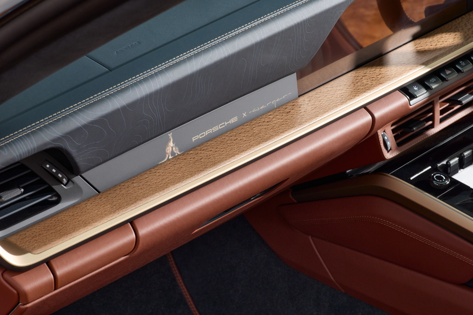 Interior dashboard detail of a Porsche 911 Turbo S 'Land Down Under' special edition, showing a kangaroo emblem and 'Porsche x Werger' branding on the trim panel, with tan leather and gold accents