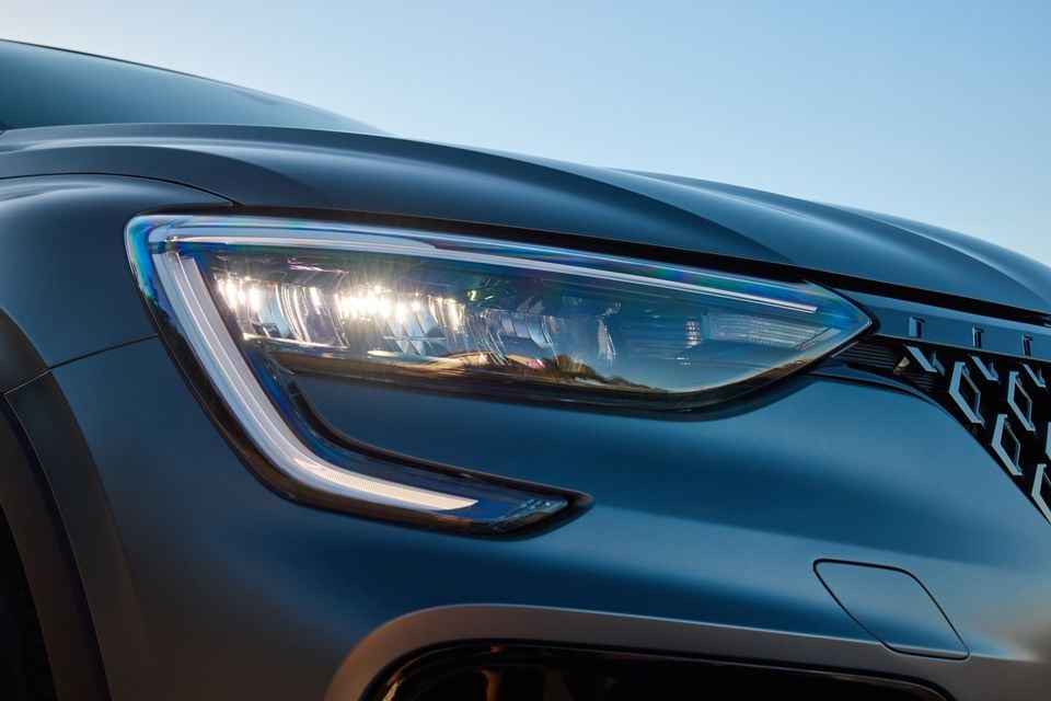 Close-up of the LED headlight on a 2026 Renault Arkana, showing the light unit and part of the front grille against a blue sky.