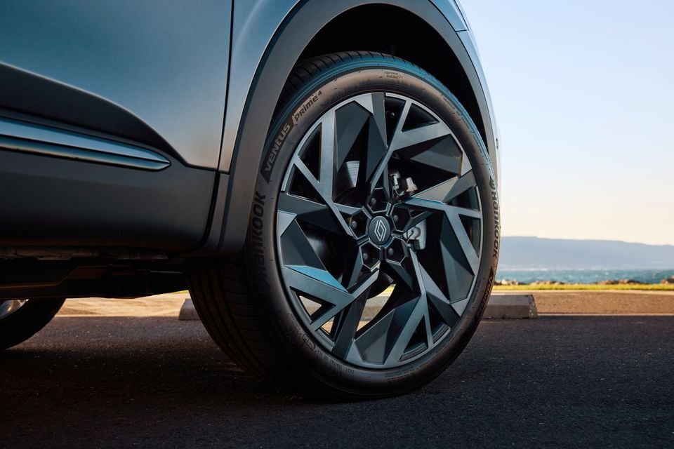 Close-up of a dark alloy wheel with Hankook Ventus Prime4 tyre on a grey Renault Arkana SUV, parked near a coastal backdrop.