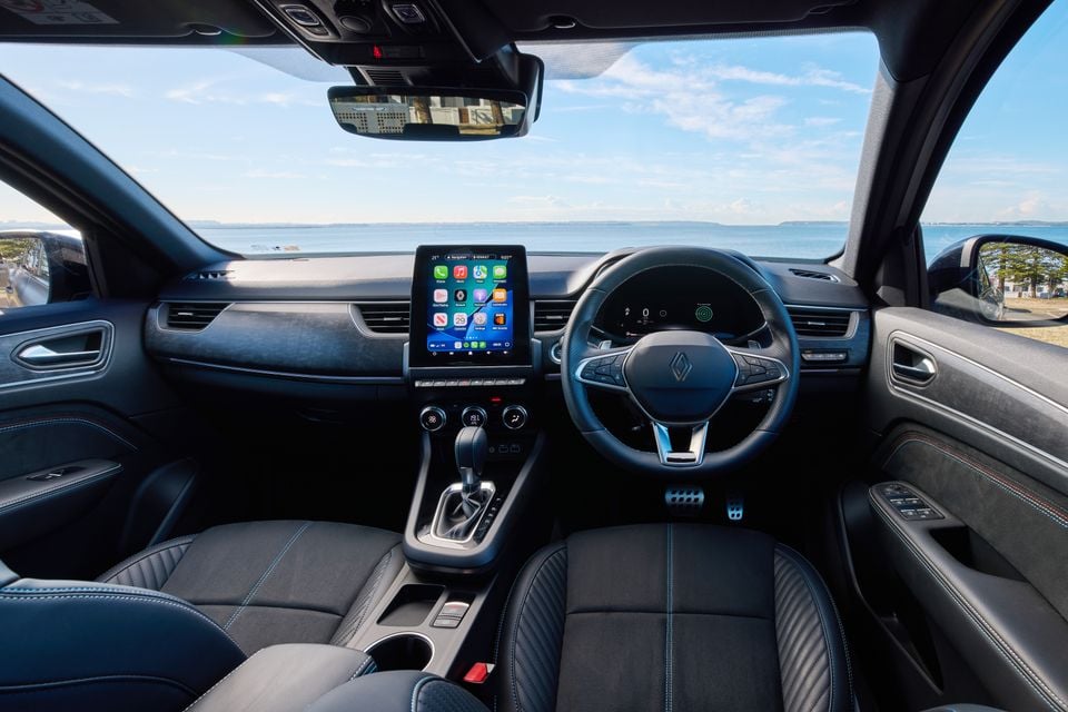 Interior of a 2026 Renault Arkana showing the dashboard, vertical touchscreen infotainment display with Apple CarPlay, steering wheel, and front seats with blue contrast stitching