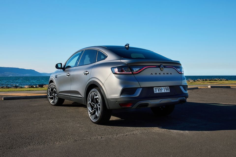 A grey 2026 Renault Arkana SUV coupe seen from the rear three-quarter angle, parked near a waterfront on a clear day.