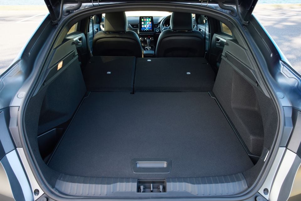 Boot of a 2026 Renault Arkana with rear seats folded flat, showing a large expanded cargo area with carpeted floor and the infotainment screen visible in the background