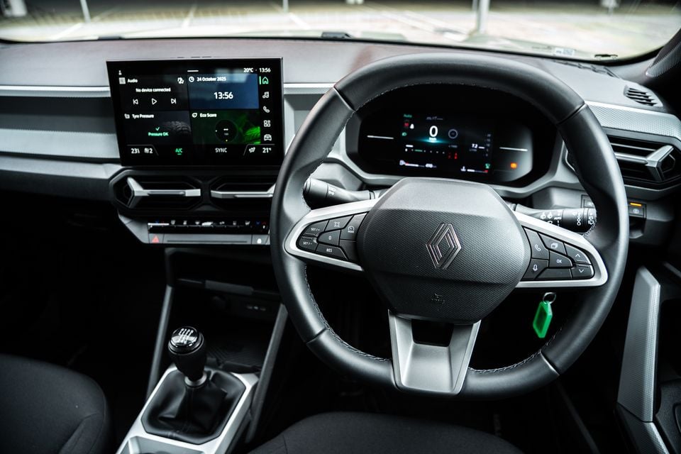 Interior of a 2026 Renault Duster showing the steering wheel with Renault logo, digital instrument cluster, touchscreen infotainment display, and manual gear shifter
