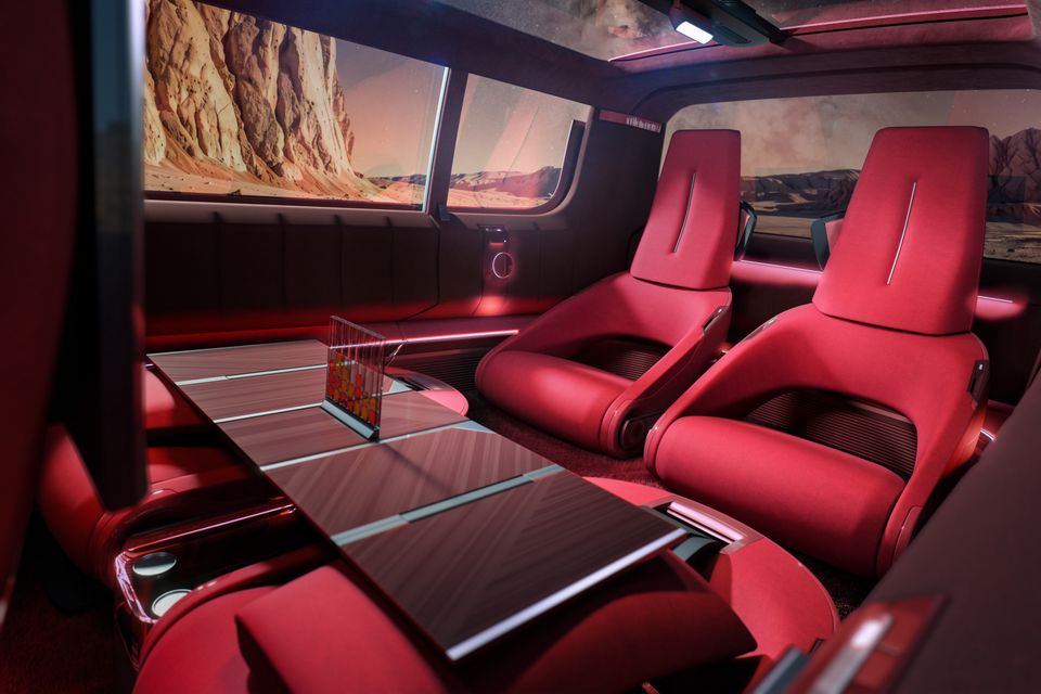 Red lounge-style cabin of the 2026 Renault Estafette concept van with swivel front seats, a wood-look table and desert scenery beyond the windows