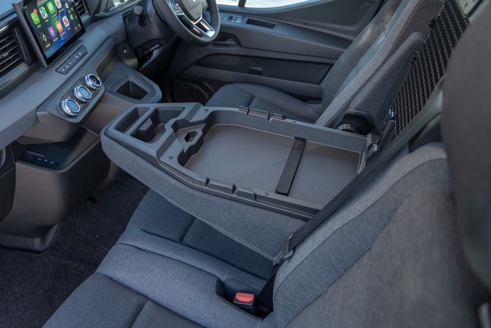 Interior of a 2026 Renault Master van showing the centre console storage tray folded out between the front seats, with the dashboard, touchscreen infotainment system and steering wheel visible in the background.