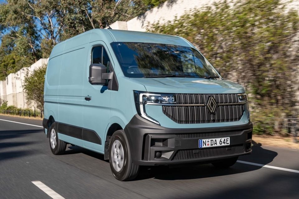 A light blue 2026 Renault Master van driving on a road, seen from the front-side