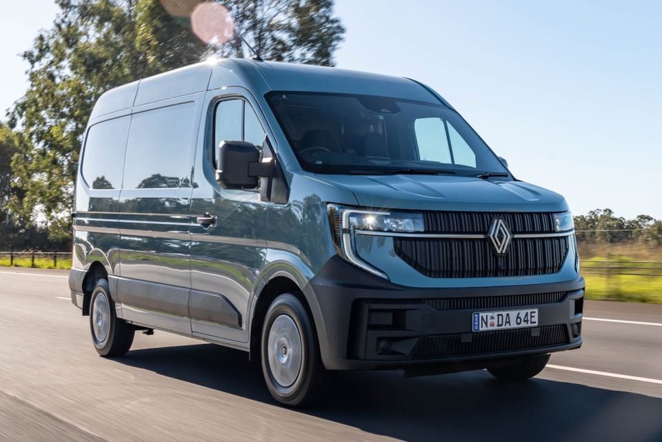 A grey 2026 Renault Master van driving on a road, seen from the front-side