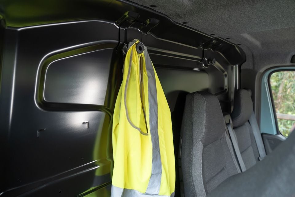 A yellow high-visibility vest hanging on an interior hook inside a van's cargo area, with seating visible in the background