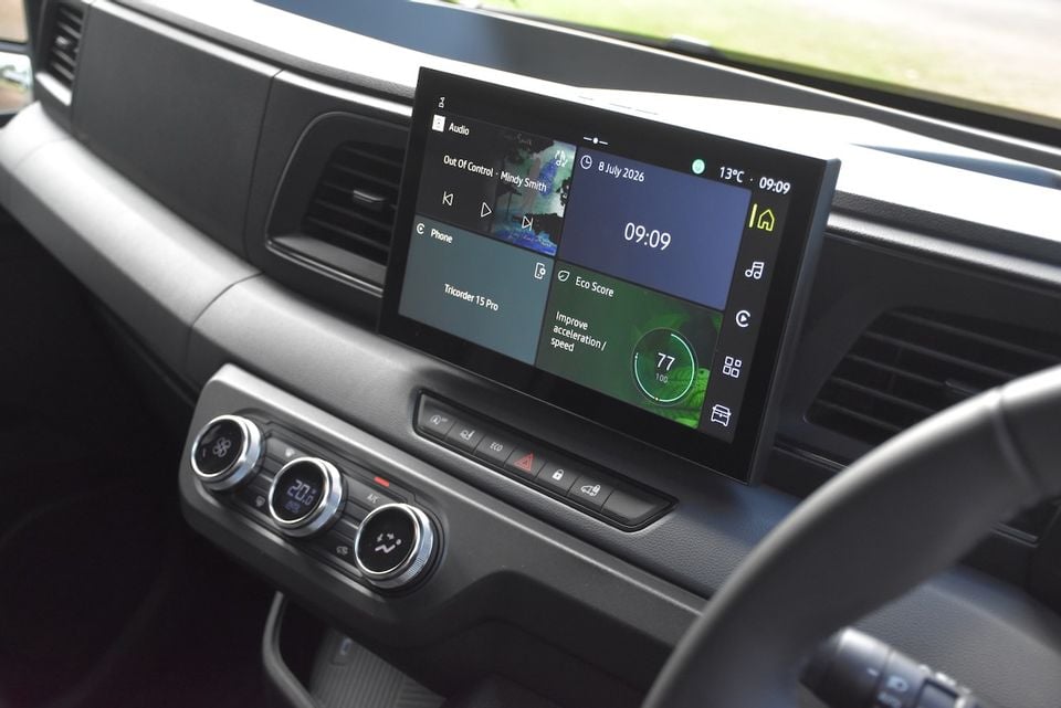 Interior view of the 2026 Renault Master dashboard showing the touchscreen infotainment system displaying audio, phone, clock and eco score widgets, with climate control dials below