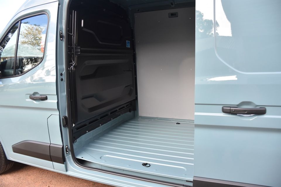 The open sliding side door of a light blue Renault Master van revealing an empty cargo area with a metal floor and white panel lining