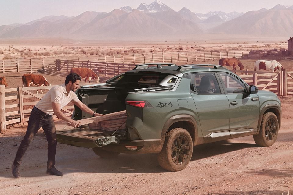 A man unloading timber planks from the tray of a green 2026 Renault Niagara 4x4 ute at a rural farm property, with cattle and mountains in the background