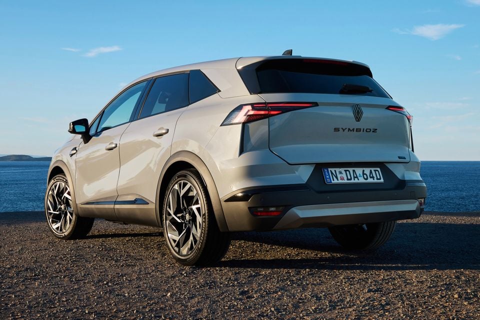A silver Renault Symbioz SUV seen from the rear three-quarter angle, parked on a gravel surface near the coast.