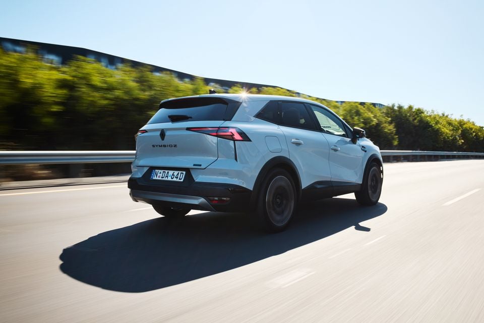A white 2026 Renault Symbioz SUV seen from the rear three-quarter angle while driving on a highway