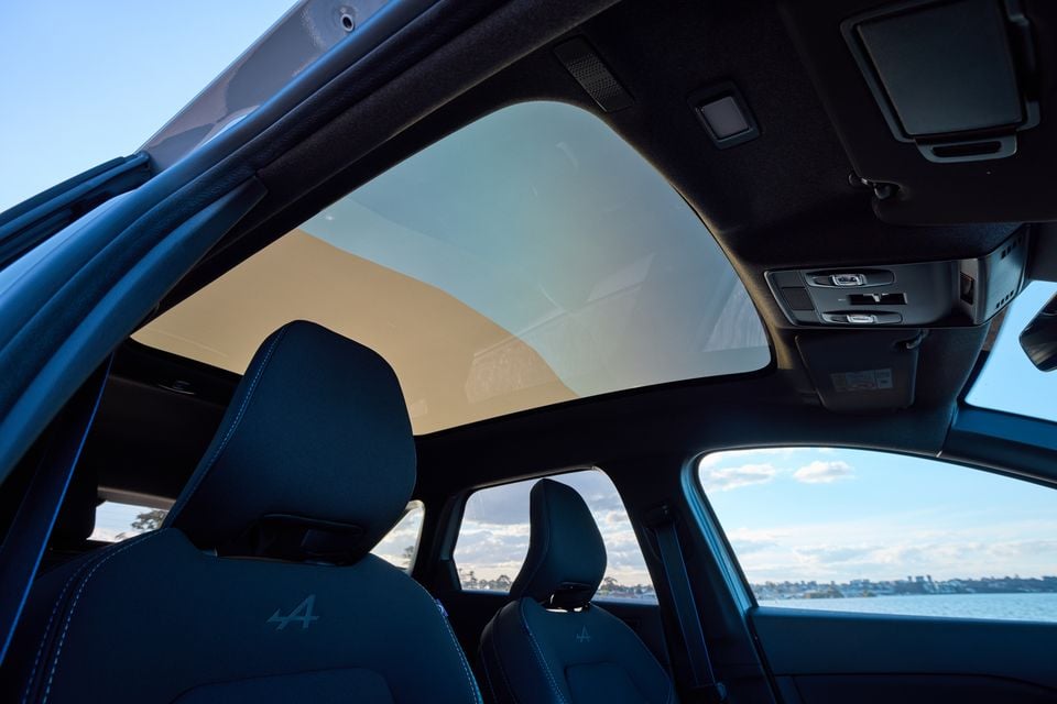 Interior view of the 2026 Renault Symbioz Esprit Alpine showing the large panoramic sunroof, dark blue Alpine-branded seats with blue stitching, and overhead console