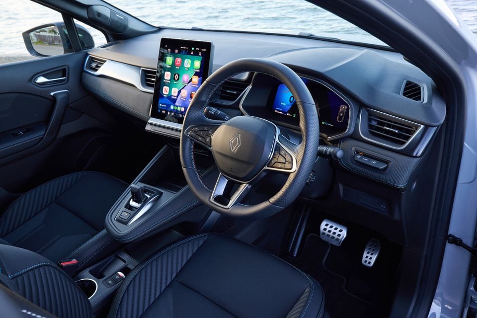 Interior of a 2026 Renault Symbioz Esprit Alpine showing the steering wheel, large portrait touchscreen infotainment display, digital instrument cluster, dark fabric seats with blue stitching, and centre console