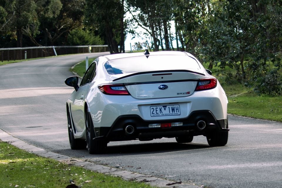 Rear view of a white Subaru BRZ tS coupe driving on a road lined with trees, with a Victorian number plate visible