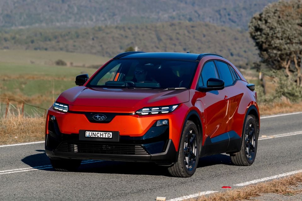 A red and orange 2026 Subaru Uncharted AWD SUV seen from the front-side on a rural road
