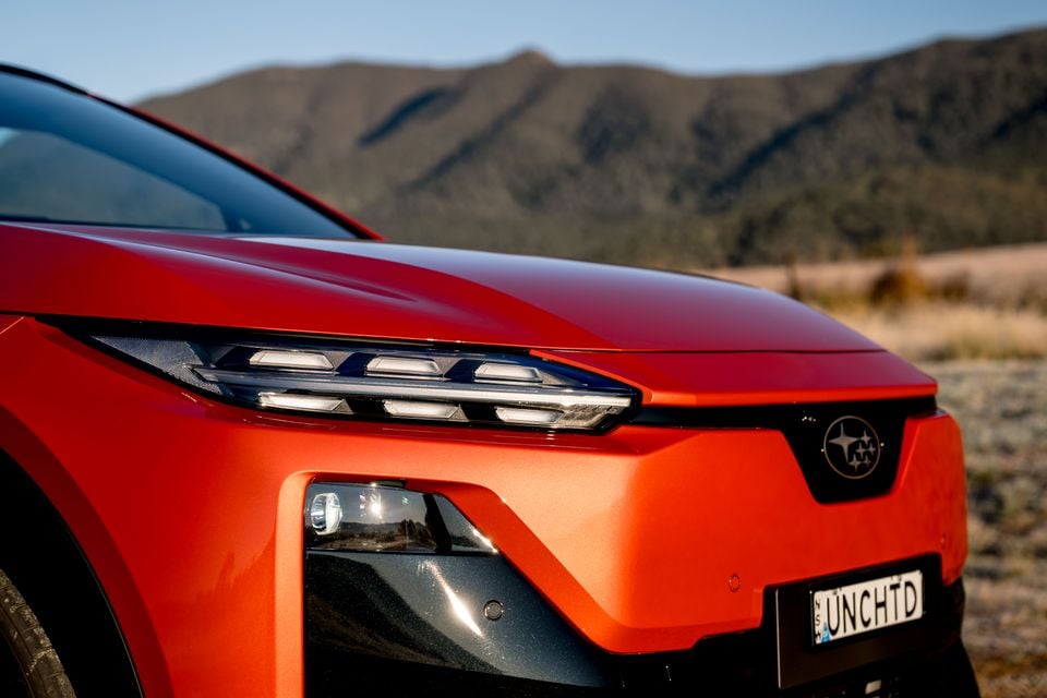 Close-up of the front end of a red Subaru Uncharted SUV, showing the LED headlights and Subaru badge, with mountains in the background