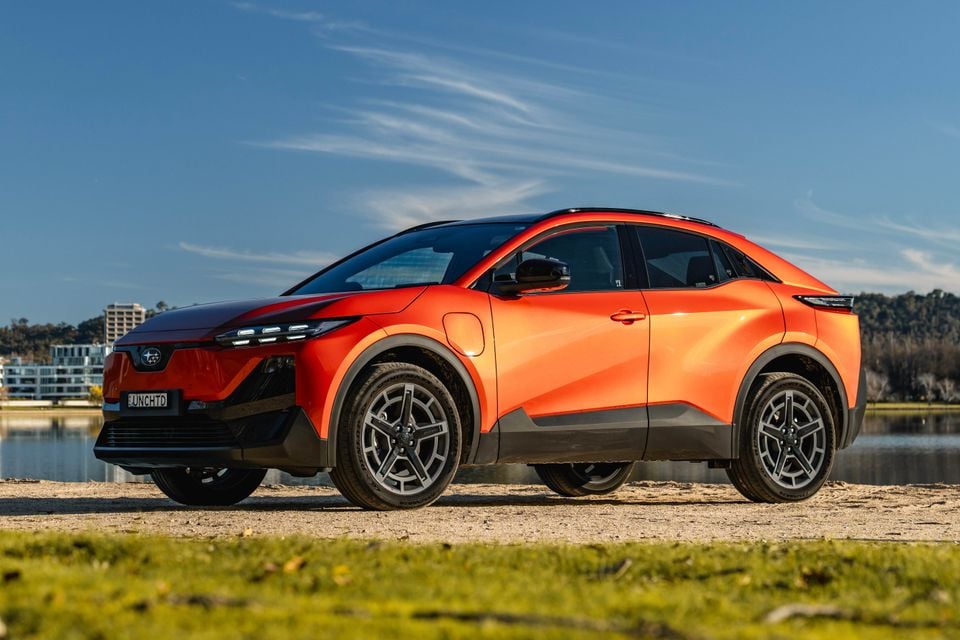 A orange 2026 Subaru Uncharted AWD SUV seen from the front-side, parked near a waterfront on a sunny day.