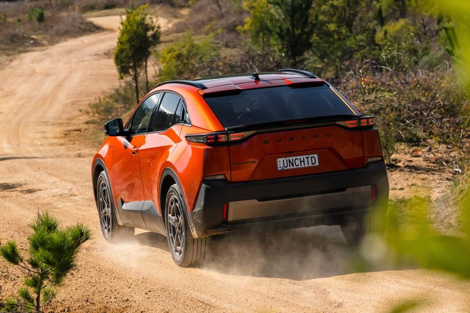 A orange Subaru Uncharted SUV seen from the rear, driving along a dusty dirt track surrounded by bushland