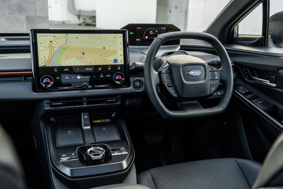 Interior of a Subaru Solterra showing the large touchscreen infotainment display with navigation, steering wheel with Subaru logo, digital instrument cluster, and centre console