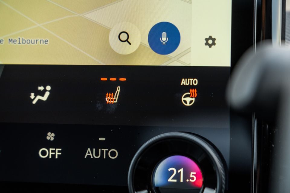 Close-up of a car's centre console showing heated seat controls, auto heated steering wheel, climate control panel set to 21.5 degrees, and a navigation map display showing Melbourne