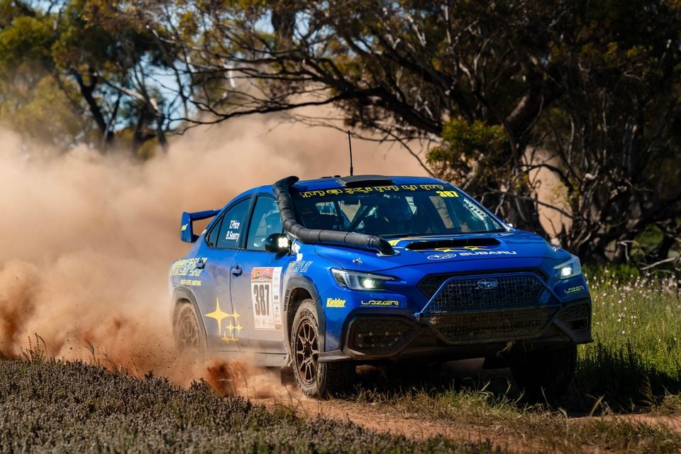 A blue Subaru WRX rally car numbered 387, driven by Toby Price, kicking up dust on a dirt track during the Sunraysia Safari Rally