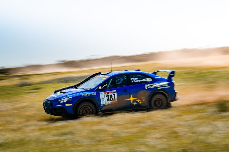 A blue Subaru WRX rally car with race number 387 and Powerplay livery speeding across a dusty dirt stage during the Sunraysia Safari Rally