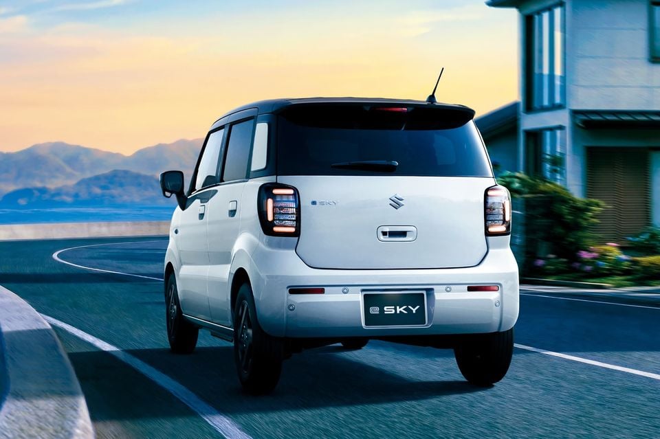 Rear view of a white Suzuki e Sky small hatchback driving on a road at sunset