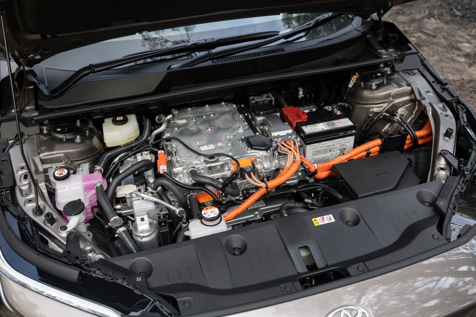 Toyota bZ4X PHEV hybrid powertrain under an open bonnet, showing orange high-voltage cables, electric motor unit, and 12V battery