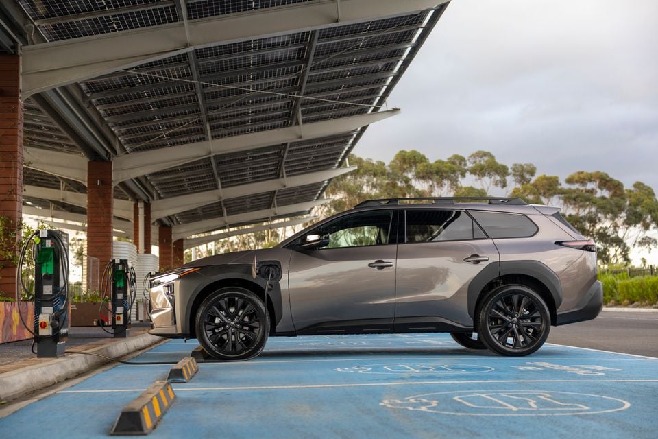 A grey 2026 Toyota bZ4X PHEV SUV plugged in and charging at a solar-canopied EV charging station