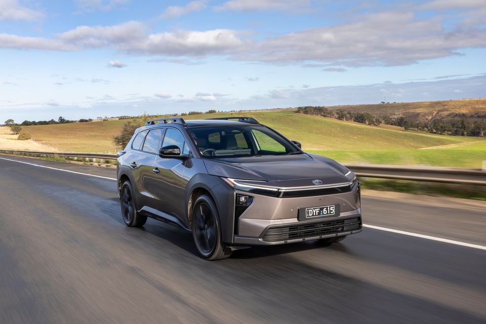 A grey 2026 Toyota bZ4X PHEV SUV driving on a highway through rolling green hills