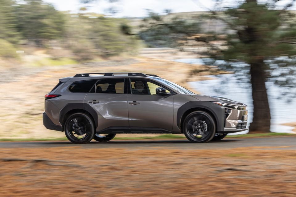 A grey 2026 Toyota bZ4X PHEV SUV driving along a rural road, seen from the side