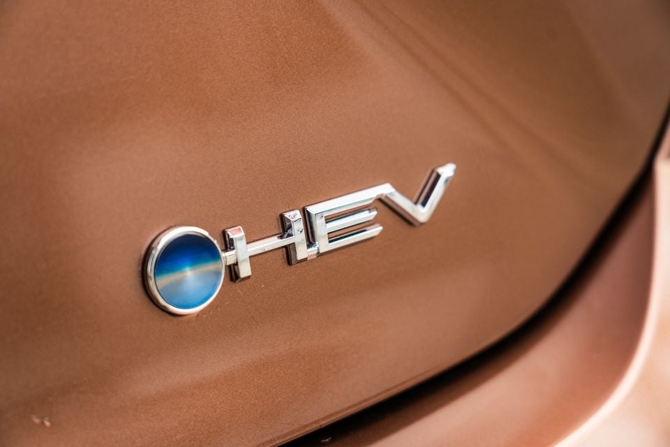 Close-up of the chrome HEV hybrid badge with a blue circular emblem on the bronze rear of a 2026 Toyota Camry SL