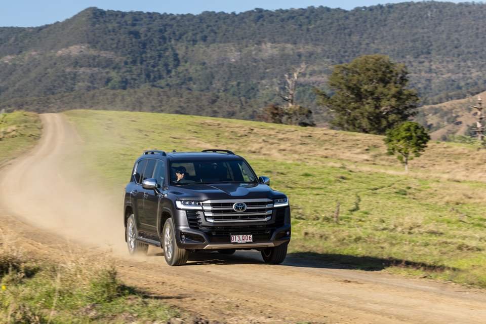 A black Toyota LandCruiser 300 Series SUV driving along a dusty gravel road through green rolling hills